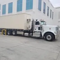 Truck with a beige container parked near a building