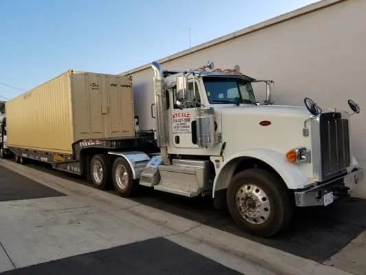 Truck carrying a beige container near a building