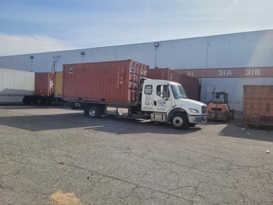 Truck transporting a red shipping container at a warehouse